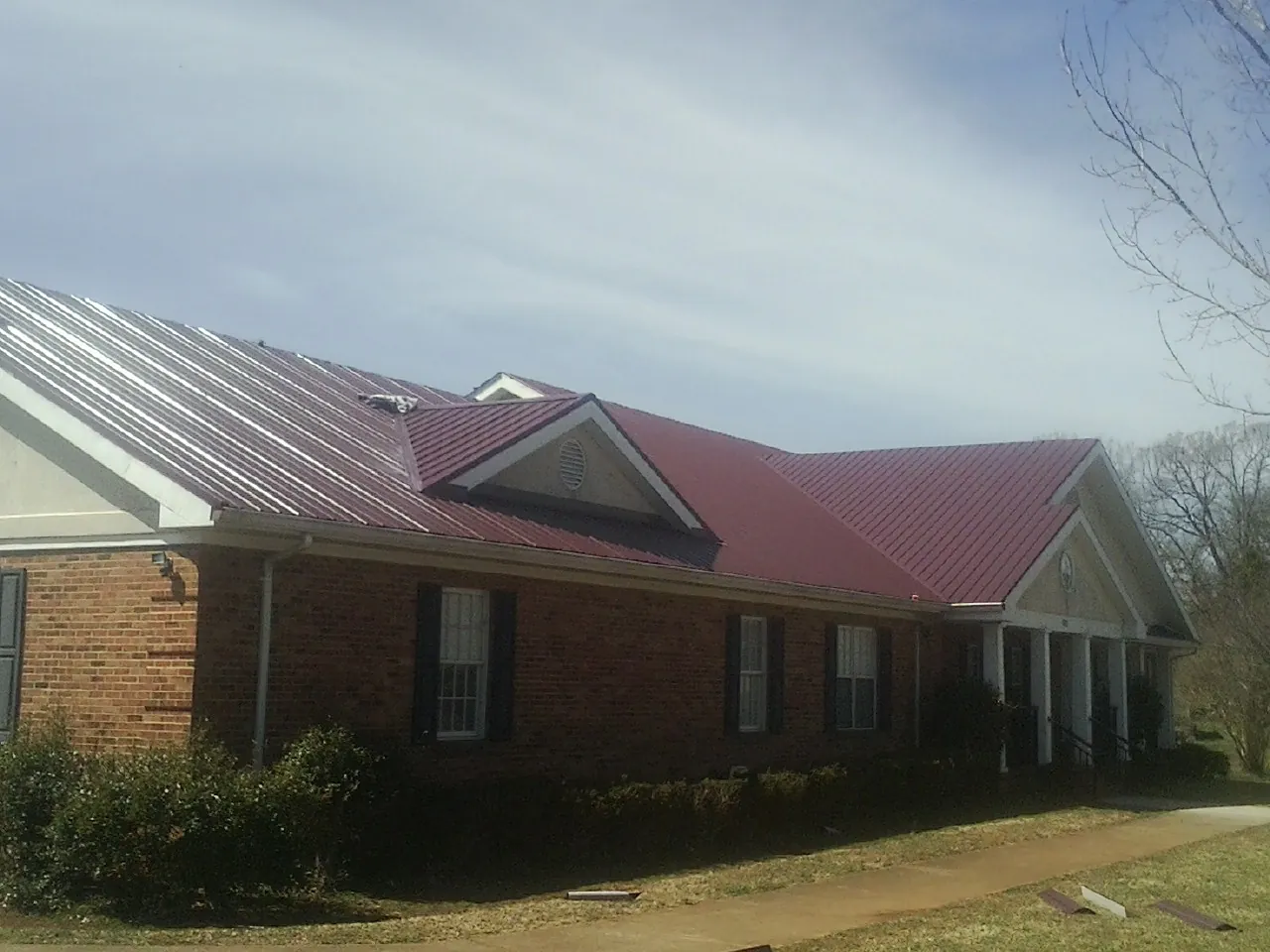 Red metal roof with gabled entries on a long brick building, from a Hail Damage Roof Repair job in Sequim