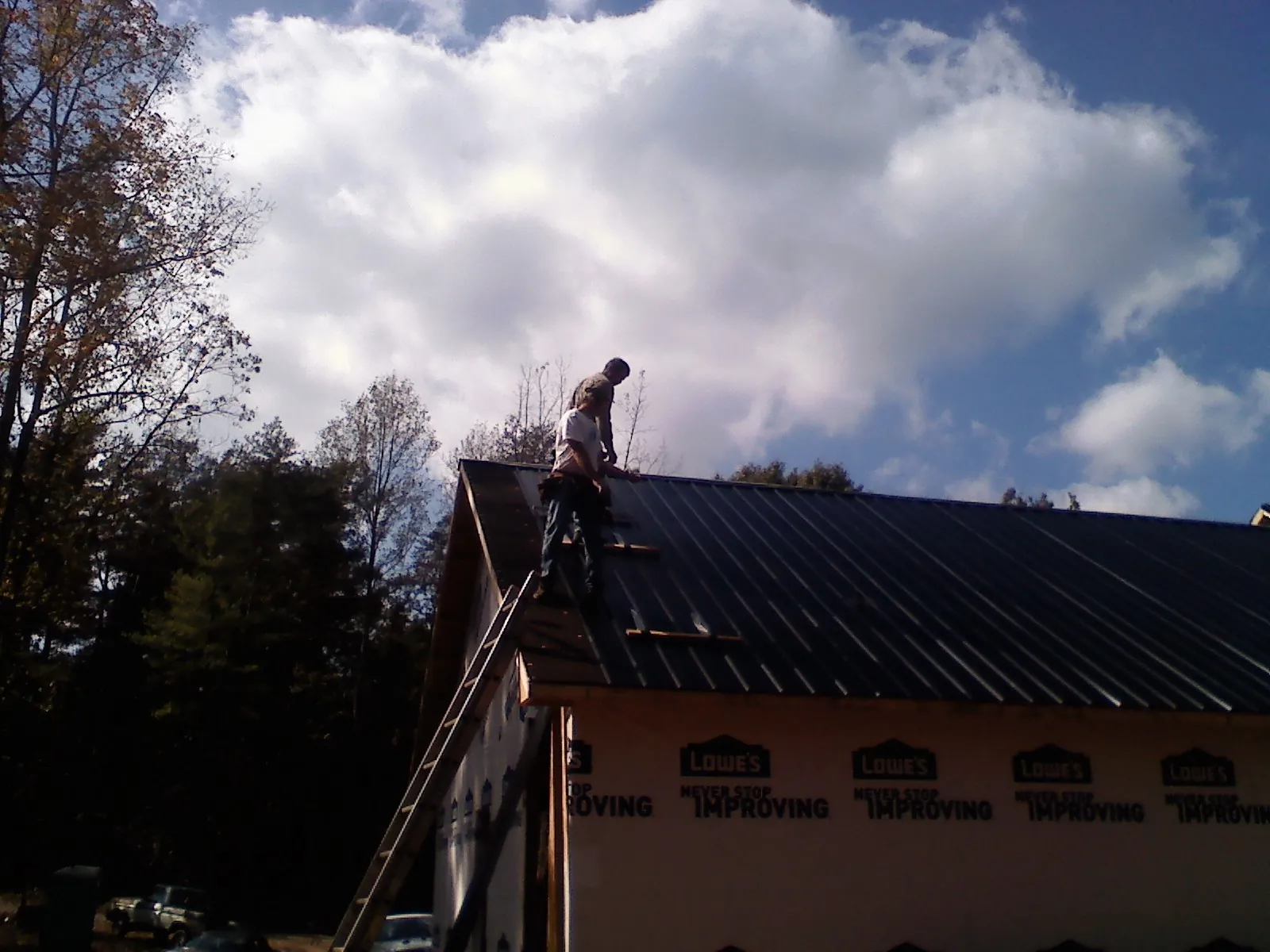 Roofer fastening dark metal panels high against a cloudy sky, from a Roof Inspection job in Sequim